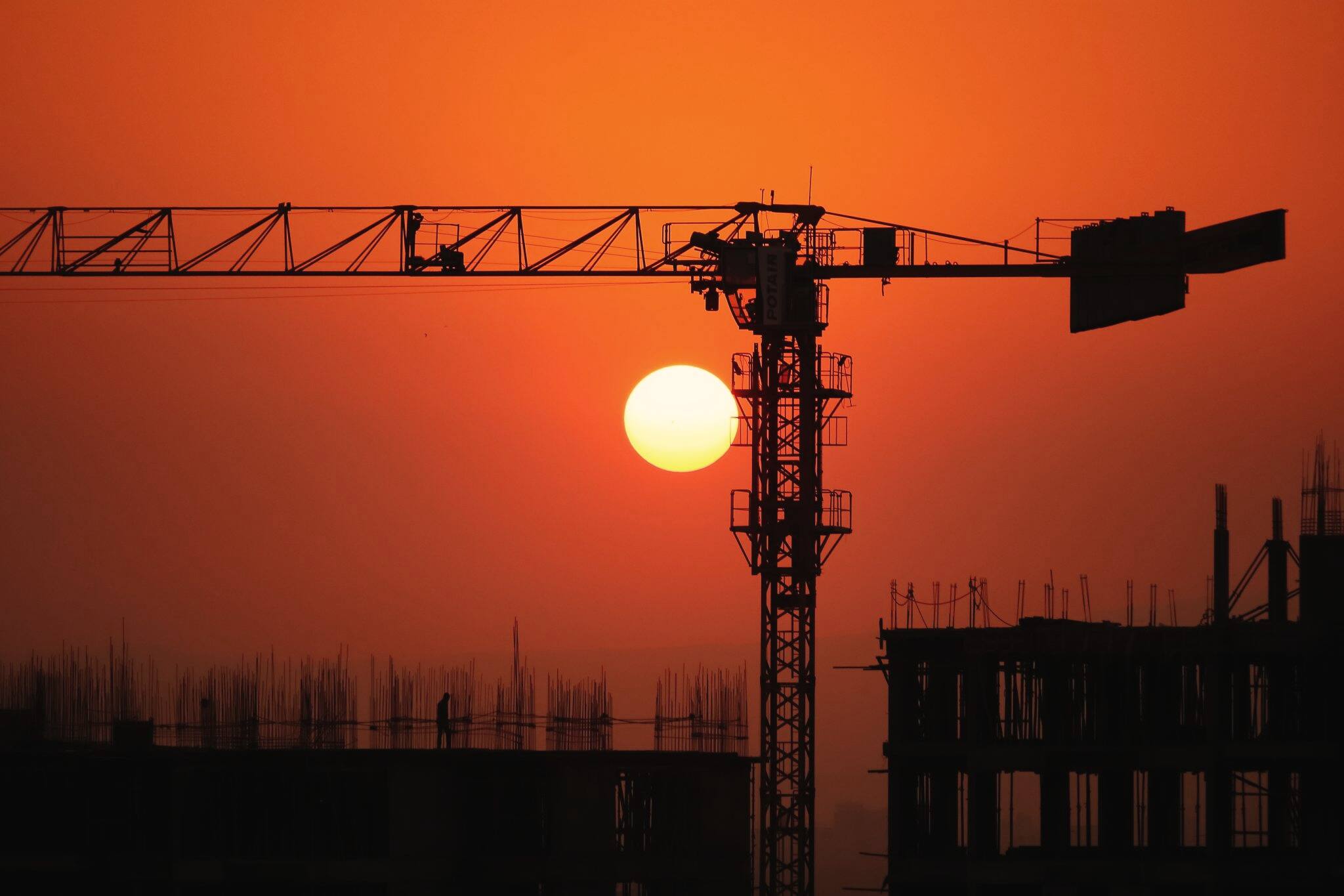 Silhouette of a tower crane over a half-built building at sunset